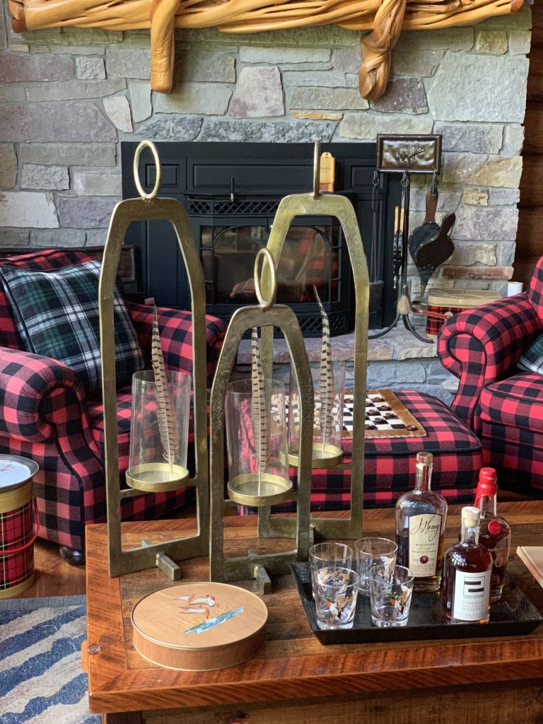 Buffalo Plaid Chairs by the fire, brass hurricane lanterns hold pheasant feathers