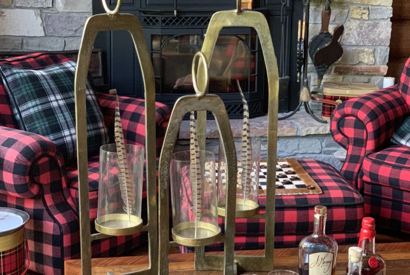 Buffalo Plaid Chairs by the fire, brass hurricane lanterns hold pheasant feathers