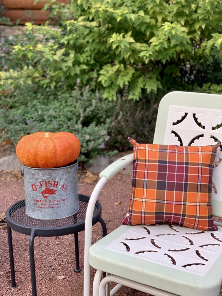 Fall plaid pillows a chair in oranges and reds and a pumpkin in a minnow bucket