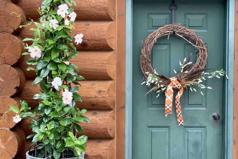 Green door with fall wreath and trellis of vine with white flowers