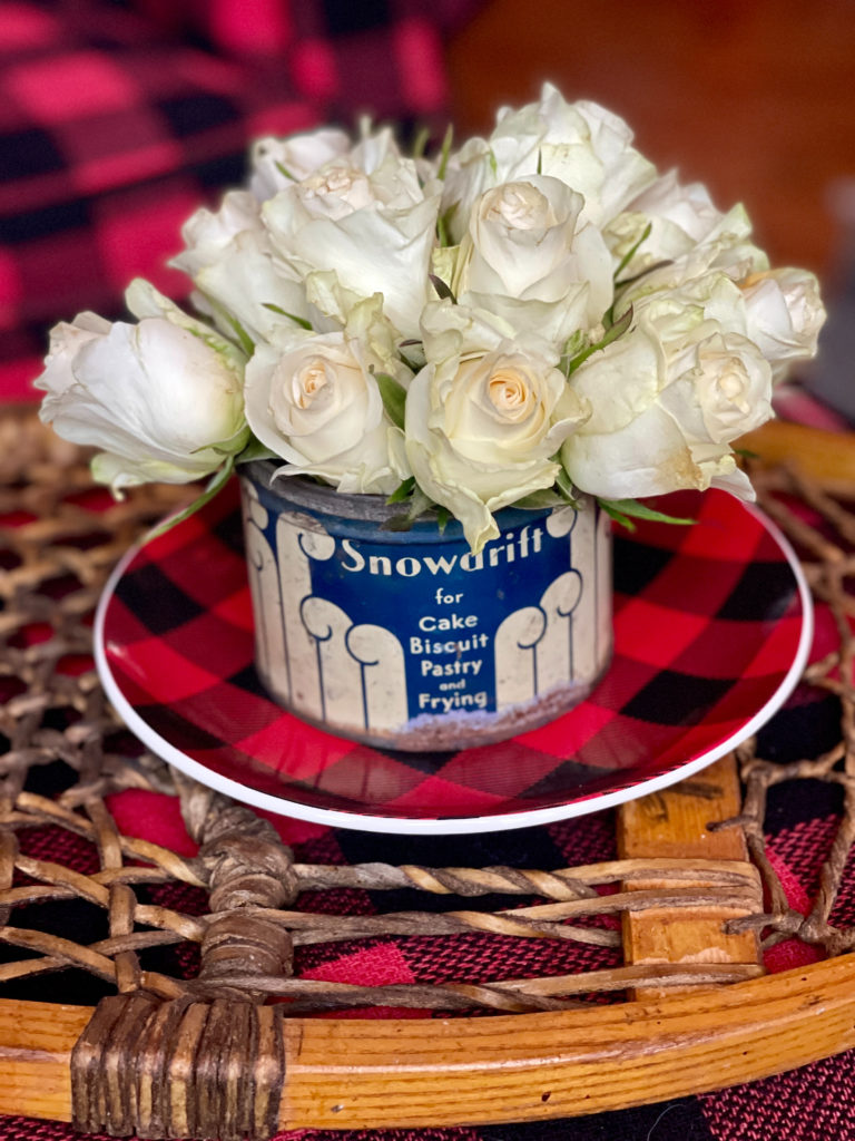 Winter decor of roses in Vintage Snowdrift Tin on buffalo plaid plate on snowshoe tray